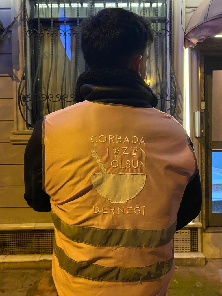 Sırtında Çorbada Tuzun Olsun Derneği logosu bulunan turuncu yelekli gönüllü